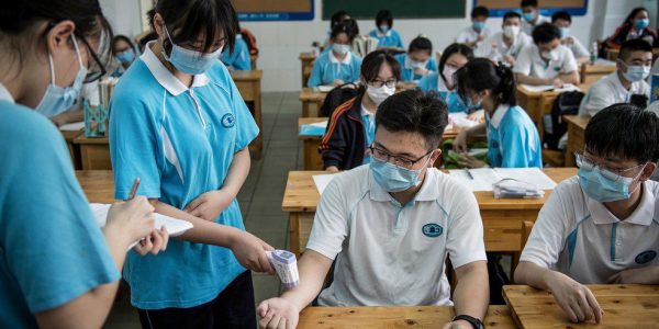 Aluna verifica temperatura de colegas de classe em Wuhan, na China, onde as escolas secundárias reabriram em 10 de julho, após o prazo ter sido adiado devido ao surto do coronavírus — Foto: STR/AFP